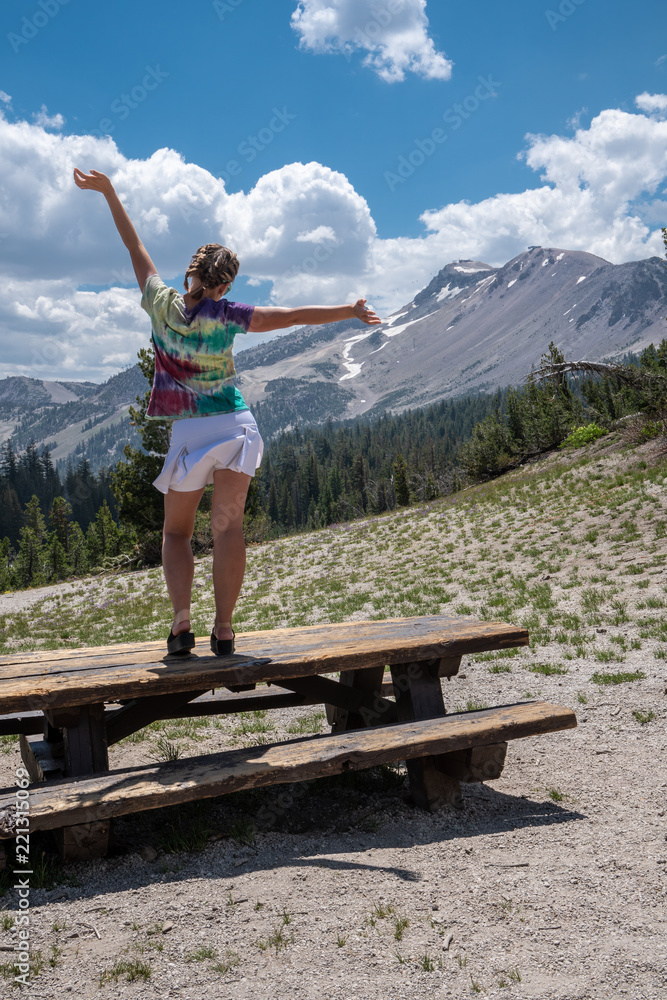 Naklejka premium Adult woman stands on top of a picnic table on a hill near Minaret Vista in Mammoth Lakes California.