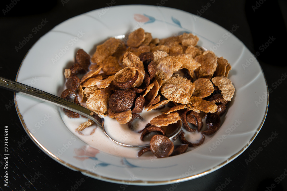 Breakfast. Sereal flakes  in white plate with milk. Black table.
