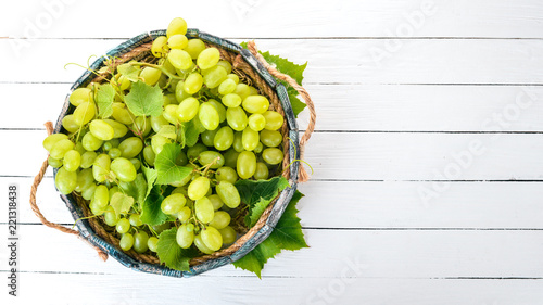 White Grapes in a wooden box on a white wooden table. Leaves of grapes. Top view. Free space for text.