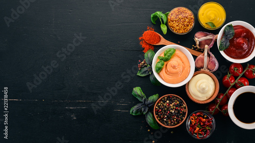 Set the sauces on a black wooden background. Ketchup, mayonnaise, mustard, soy sauce, barbecue sauce, pepper and spices. Top view. Free space for text.