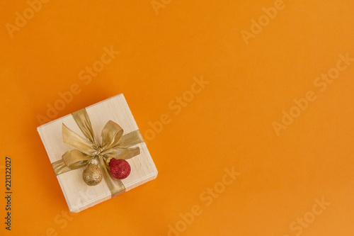 Gift or present box with golden ribbon and Christmas decoration on orange  background. Top view, copy space.