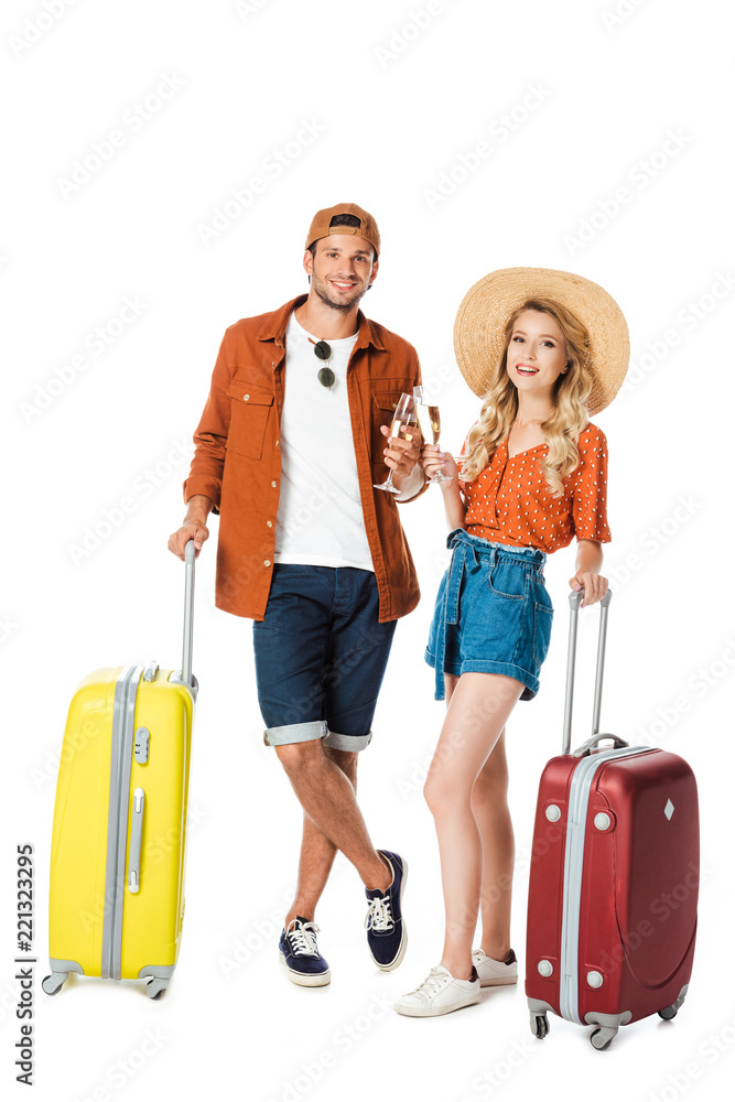 smiling couple standing with travel bags and clinking with glasses of champagne isolated on white smiling couple standing with travel bags and clinking with glasses of champagne isolated on white