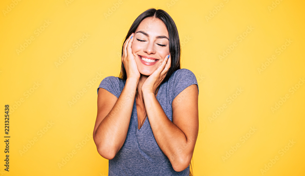 Young attractive cute brunette woman in gray T-shirt is posing and looking on camera isolated over yellow wall Young attractive cute brunette woman in gray T-shirt is posing and looking on camera isolated over yellow wall