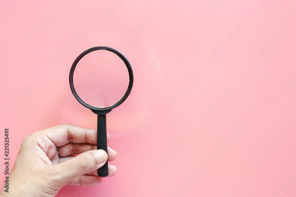 Hand holding a magnifying glass on pink background with copy space Hand holding a magnifying glass on pink background with copy space