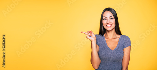 Photo of young excited beautiful happy brunette woman, girl pointing away and smile isolated on yellow background banner