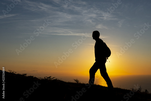 Hiker in the backlight by the mountain on the coast near the sea