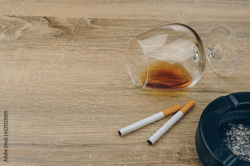 a glass of brandy, cigarettes and black ceramic ashtray full of ashes on the wooden table