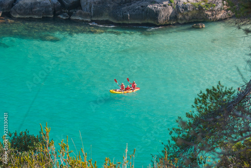 A family on a kayak in the crystalline sea of cove Macarelleta in Menorca