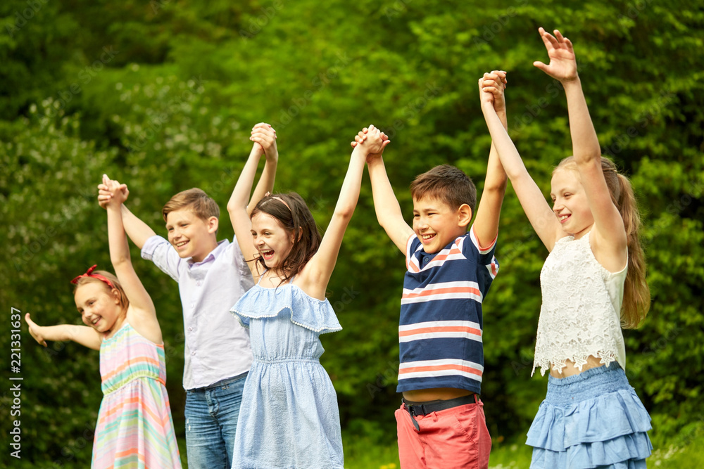 childhood and friendship concept - happy kids holding raised hands in summer park childhood and friendship concept - happy kids holding raised hands in summer park