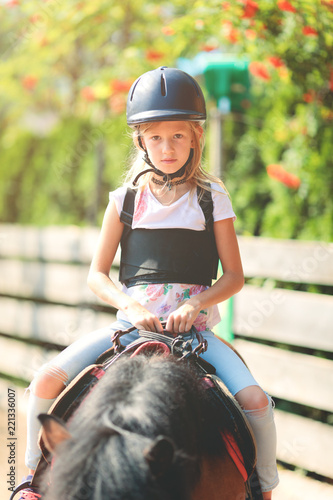 Young Caucasian girl riding on a pony, having longe line riding lesson
