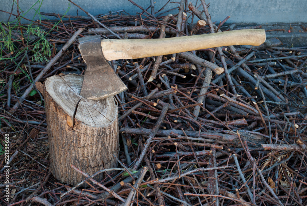 Iron ax with a wooden handle in a tree deck. Stump giving summer, against the background of branches of knots dry, sunny day Iron ax with a wooden handle in a tree deck. Stump giving summer, against the background of branches of knots dry, sunny day