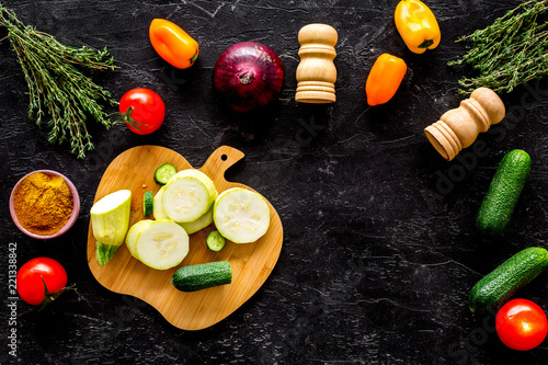 Cooking vegetable stew concept. Fresh vegetables squash, bell pepper, tomato, spices and cutting doard on black background top view space for text photo