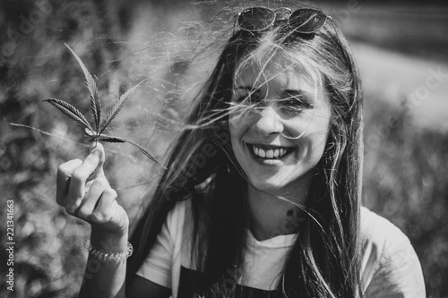 happy young woman smiling and holding a marijuana leaf outdoors