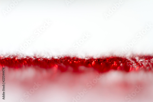 Red glitter texture on white background. Defocused.