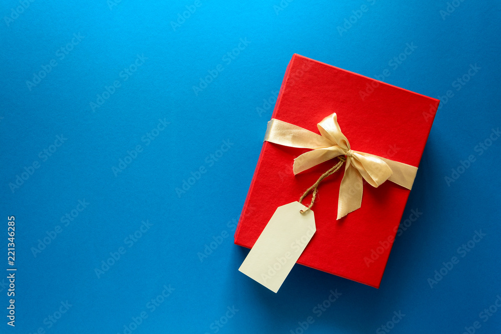 Top view on red Christmas gift box decorated with ribbon on blue paper background. New Year, holidays and celebration decorations concept. Copy space. Flat lay. Mock-up Top view on red Christmas gift box decorated with ribbon on blue paper background. New Year, holidays and celebration decorations concept. Copy space. Flat lay. Mock-up