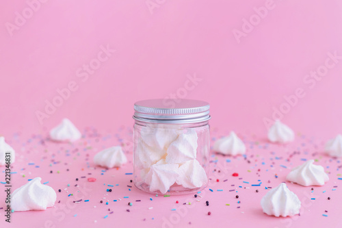 White meringues in glass jar on pink background