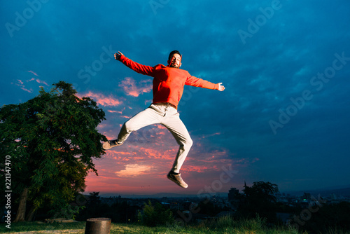 Free runner doing parkour jump. Young parkour man jumping in park on a sunrise against a blue sky