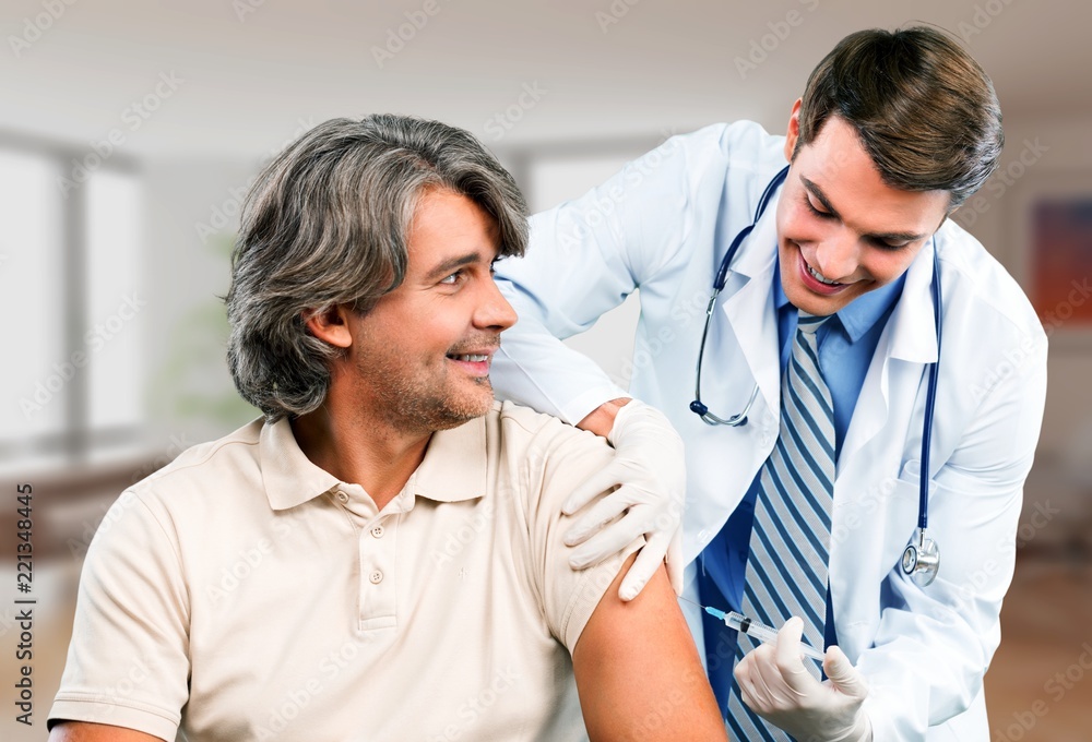 Handsome doctor making vaccination to male patient on background Handsome doctor making vaccination to male patient on background