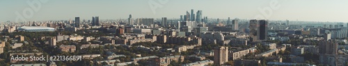 Panorama of evening summer cityscape with the residential district and dwelling houses in the foreground, multiple office skyscrapers and business high-rises in the distance; huge stadium on the left