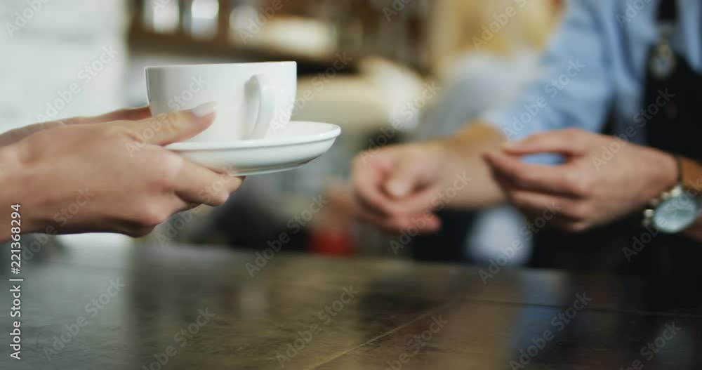 Hands of the Caucasian waiter passing cup of coffee to the female client. At the bar in the cafe. Hands of the Caucasian waiter passing cup of coffee to the female client. At the bar in the cafe.