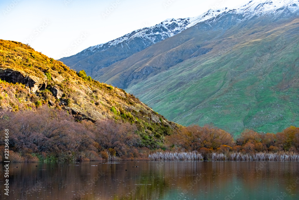 Stunning of the scenery of rocky snow mountain with the reflection of the yellow leafs tree forest in Autumn. Diamond lake track, Wanaka, New Zealand.