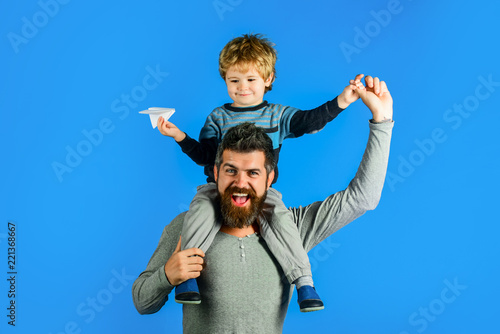 Happy kid having fun playing with paper airplane. Family leisure activity. Father and cute son launch paper plane. Developing kids creativity. Parent holds on shoulders cute boy with paper aeroplane. © Svitlana