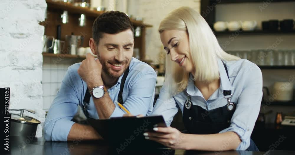 Young good looking waiter and waitress standing at the bar and making menu set, woman writing with pencil. Young good looking waiter and waitress standing at the bar and making menu set, woman writing with pencil.