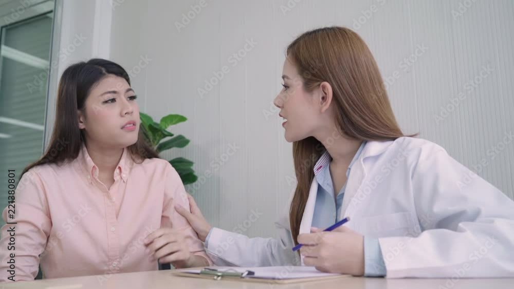 Doctor talking to unhappy teenage patient in exam room. Asian woman doctor encouragement and support to cancer patient after consult and examine health in medical clinic or hospital. Doctor talking to unhappy teenage patient in exam room. Asian woman doctor encouragement and support to cancer patient after consult and examine health in medical clinic or hospital.