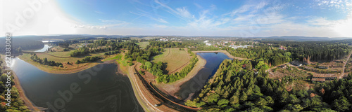 Artificial pond in the Harz Mountains with a neighbouring meadow and a small town in the background, aerial photo with the drone.