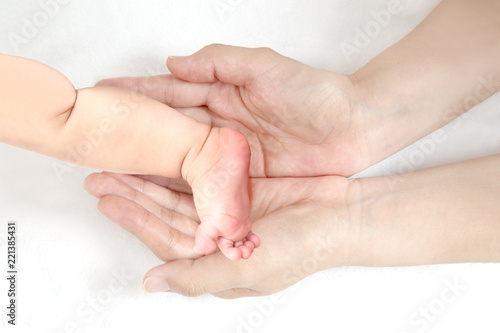 赤ちゃんの小さな片足を包むお母さんの大きな両手のアップ。成長と健康を喜ぶ母。母性、愛情、幸せ、育児、健康のイメージ © chikala