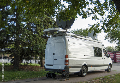 The van is equipped with a technical for television and information transfer, standing on the path surrounded by trees. photo