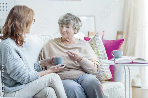 Smiling grandmother talking with friendly caregiver during meeting at home