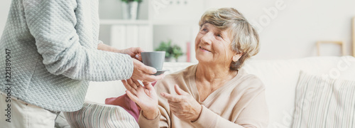 Close-up of person with cup of tea taking care of smiling senior woman