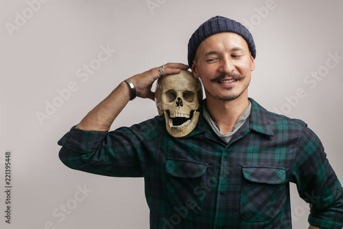Stylish happy man with mustache and knitted hat, holding scull while posing indoors, with copy space for your text or promotional content