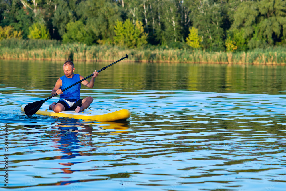 Happy man is relaxing on a SUP board on large river