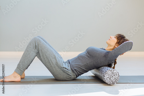 Seria photo of young caucasian female sportswoman uses a foam roller for self-massage for relaxation, stretching muscles and back pain. Girl in workout in pilates studio. photo