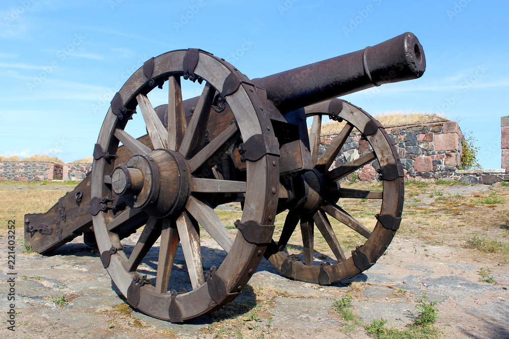 Ancient museum gun with wooden wheels in a fortress against a blue sky