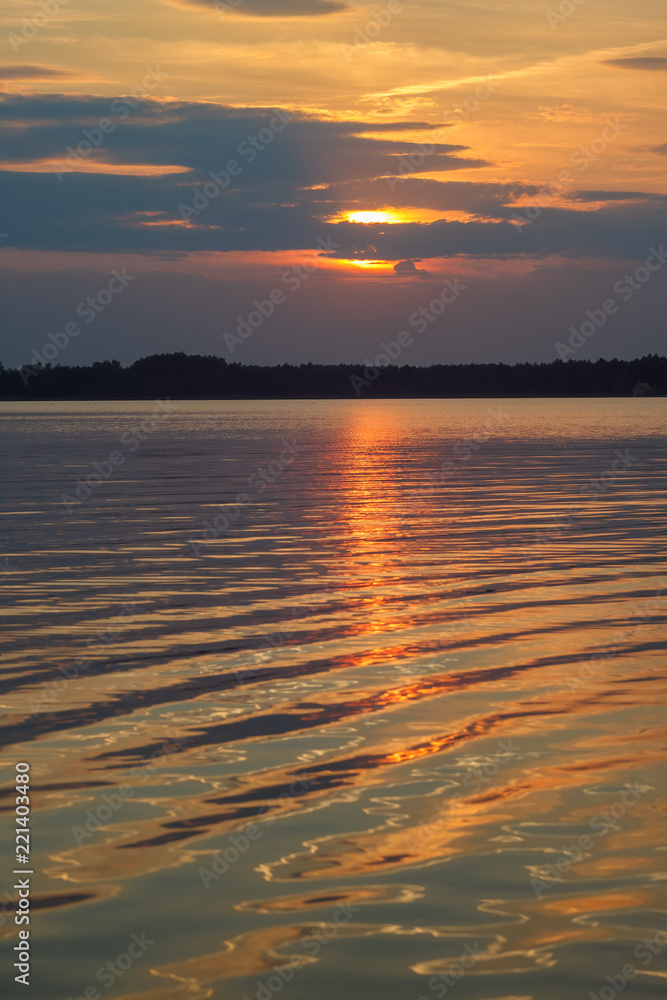 Sunset on the lake. Evening sky with beautiful clouds is reflected in the water of the lake