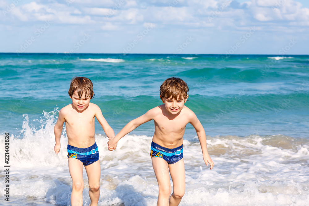 Two happy little kids boys running on the beach of ocean. Funny cute children, siblings, twins and best friends making vacations and enjoying summer on stormy sunny summer day. Miami, Florida