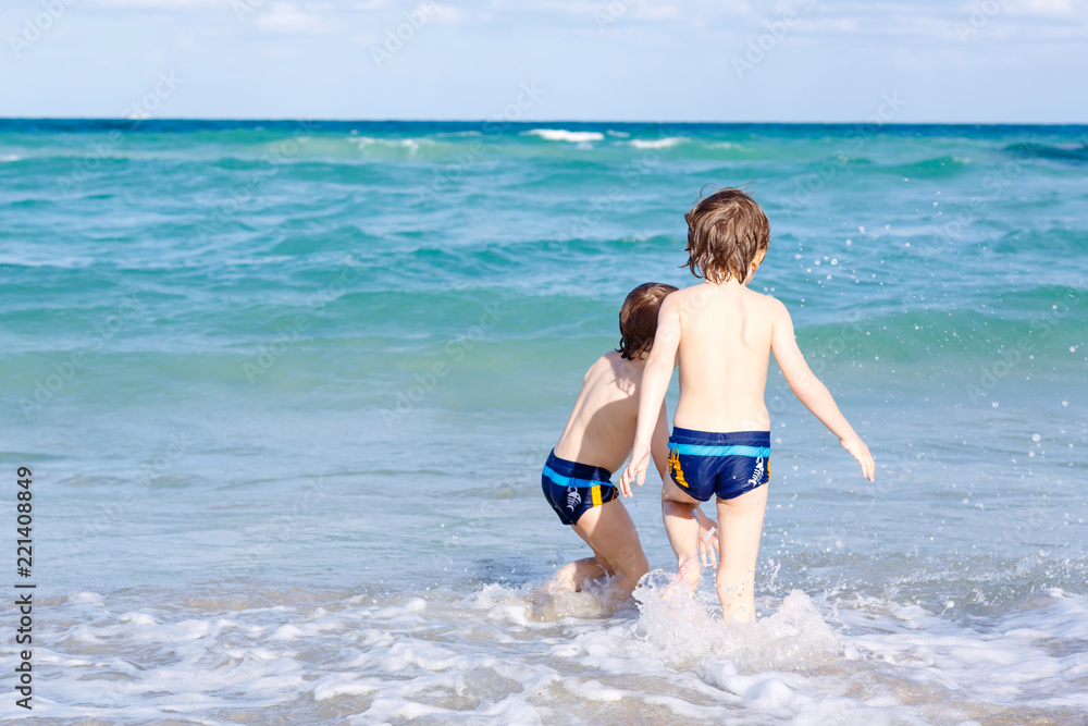 Two happy little kids boys running on the beach of ocean. Funny cute children, siblings, twins and best friends making vacations and enjoying summer on stormy sunny summer day. Miami, Florida