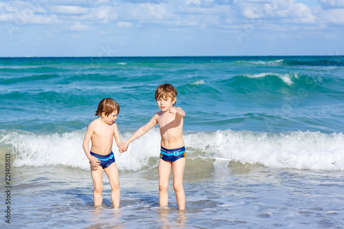 Two happy little kids boys running on the beach of ocean. Funny cute children, siblings, twins and best friends making vacations and enjoying summer on stormy sunny summer day. Miami, Florida