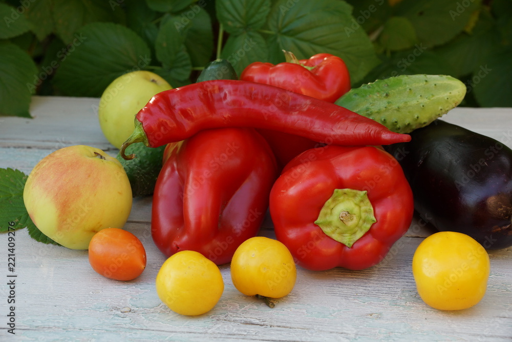 tomatoes red and yellow peppers red hot chili peppers apples cucumbers. green leaves on a white wooden table. tomatoes red and yellow peppers red hot chili peppers apples cucumbers. green leaves on a white wooden table.
