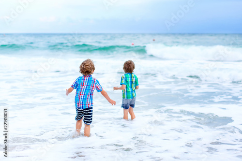 Two happy little kids boys running on the beach of ocean. Funny cute children, sibling and best friends making vacations and enjoying summer on stormy windy day in Miami, Florida, USA.