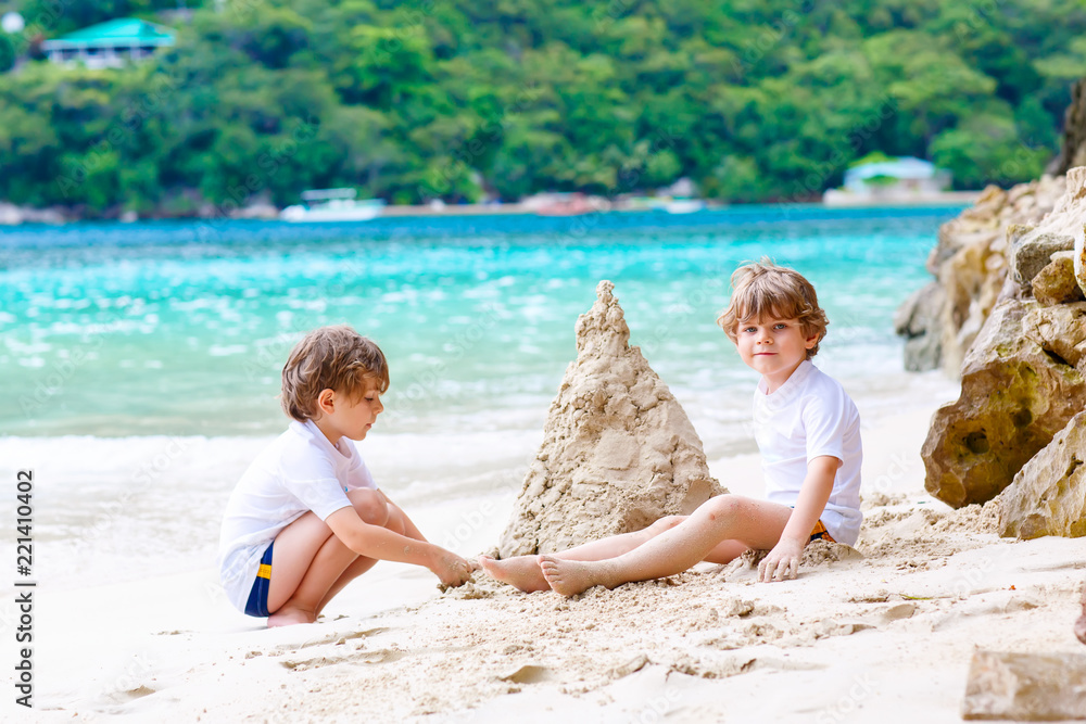 Two little kids boys having fun with building a sand castle on tropical beach of Seychelles. children playing together on their vacations Two little kids boys having fun with building a sand castle on tropical beach of Seychelles. children playing together on their vacations