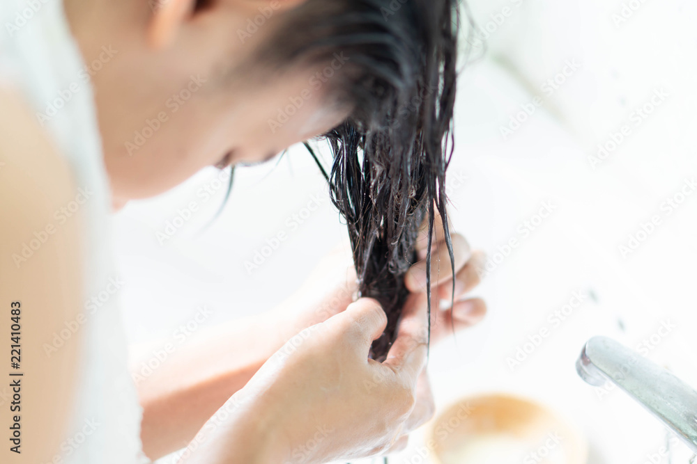 Closeup woman applying hair conditioner with over light in the bathroom, selective focus