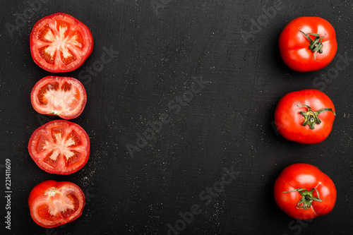 Whole tomatoes and half red tomatoes lie on black stone background. Fresh and succulents autumn vegetables, copy space