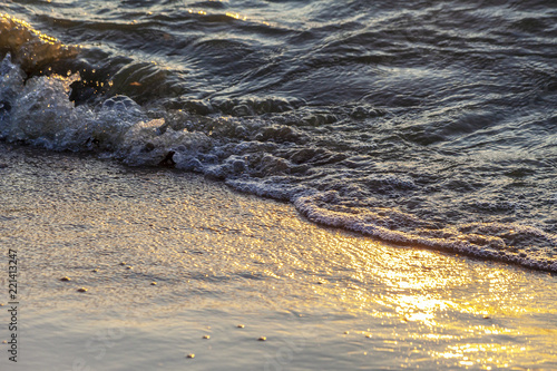 Waves on the sandy shore of a large river. The rays of light are reflected in the waves.