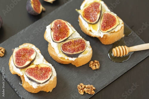 Ricotta sandwiches, fresh figs, walnuts and honey on a slate plate on a black background