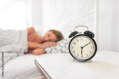 Analog alarm clock. Woman sleeping in bed