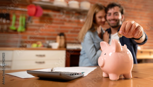 Happy couple inserting coin in piggybank photo